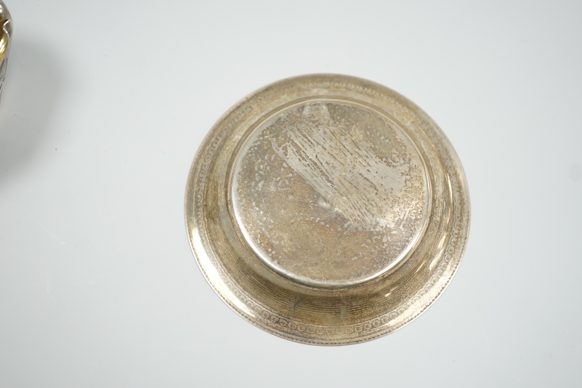 A late Victorian novelty parcel gilt silver salt modelled as a basket, with aesthetic engraved decoration, London, 1884, length 65mm, together with an Egyptian white metal small dish.